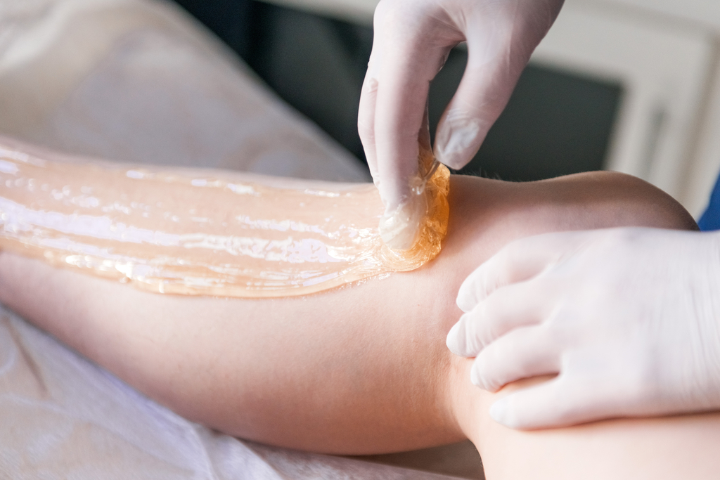 Esthetician wearing medical gloves applies wax to a client's lower leg.